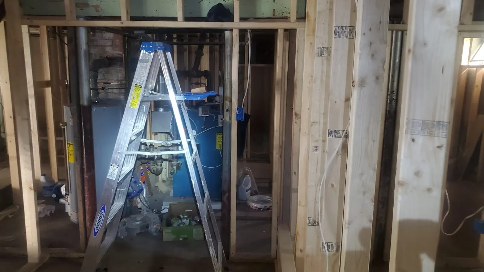 Carpenter in Lynn, MA framing a basement with a ladder and exposed studs